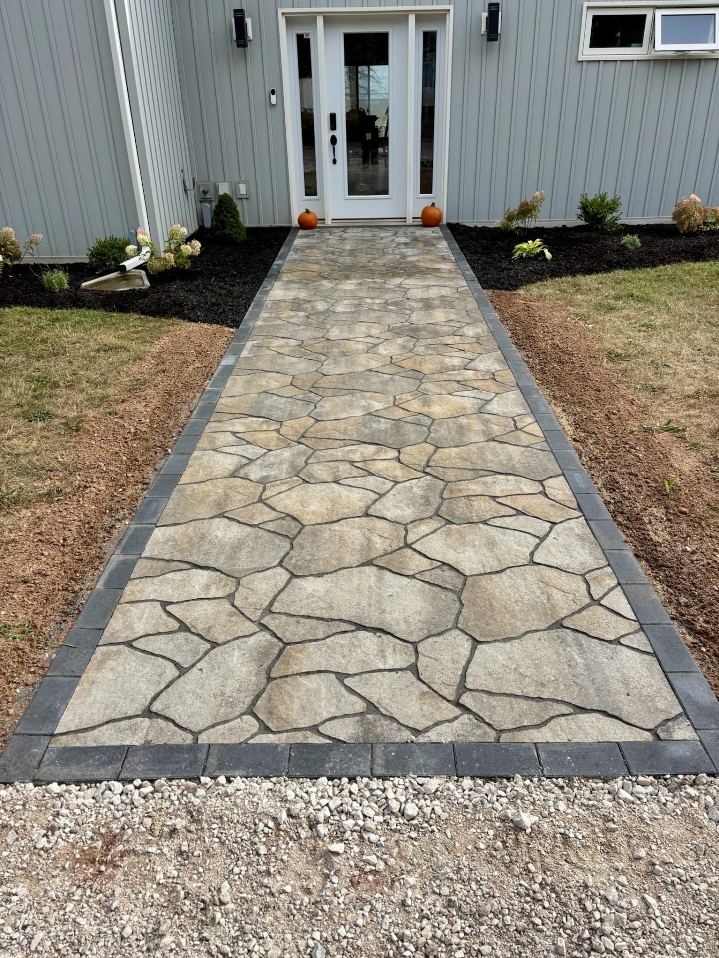 Stone walkway leading to house entrance with pumpkins.