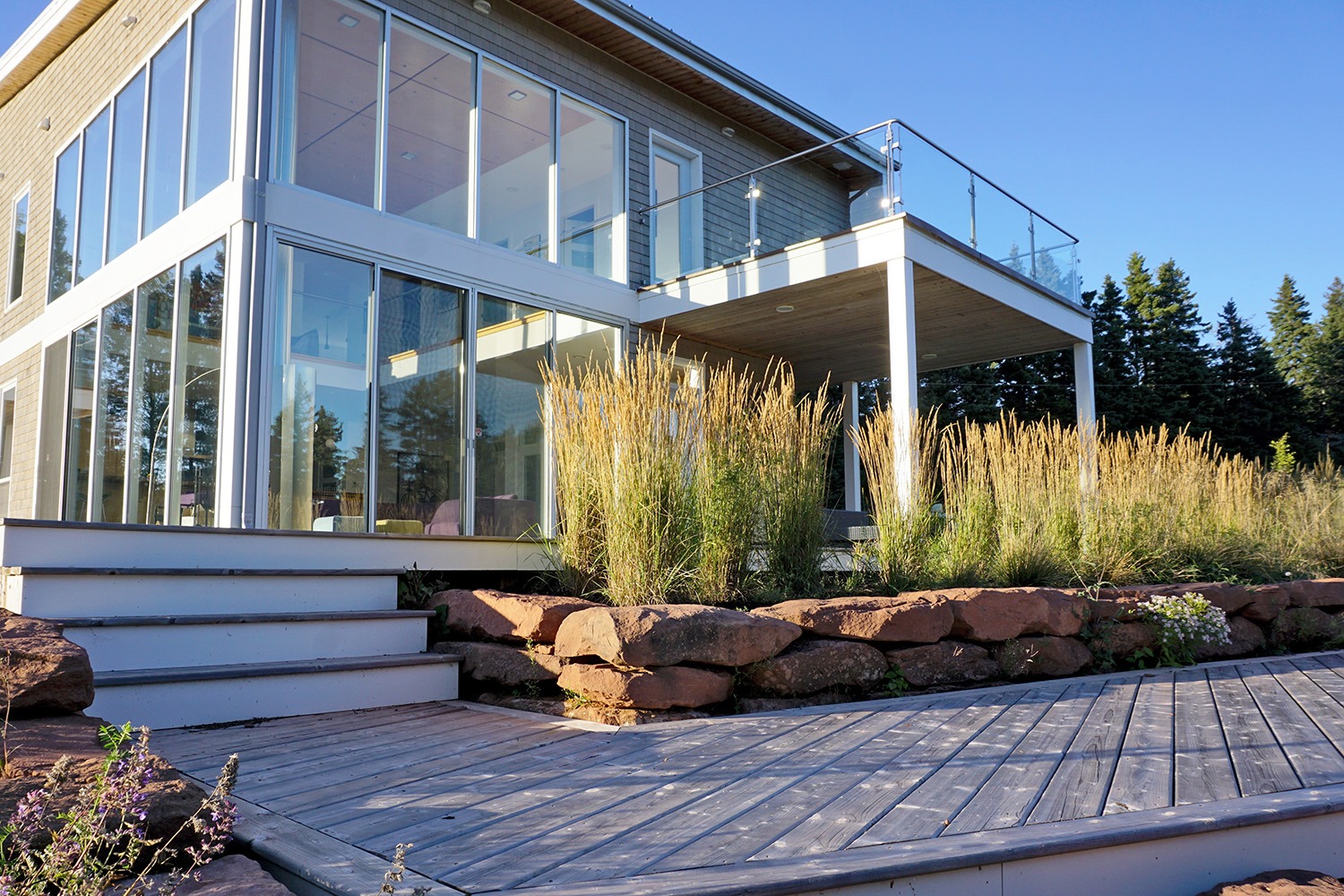 Modern glass house with wooden deck and steps.