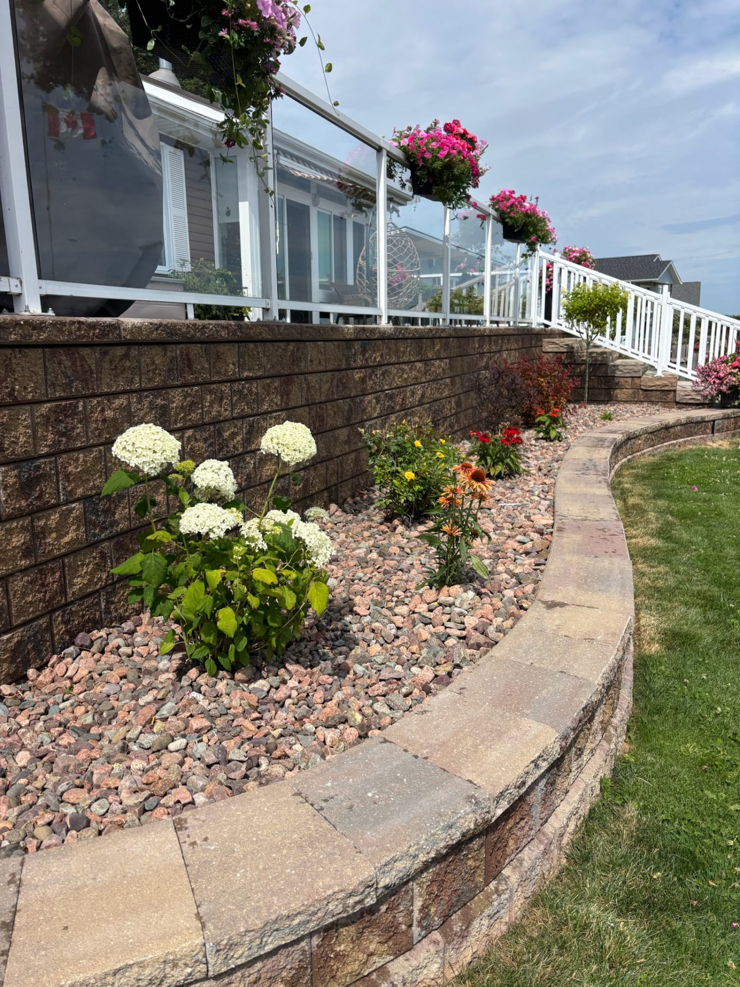 Colorful garden with flowers, rocks, and glass railing.