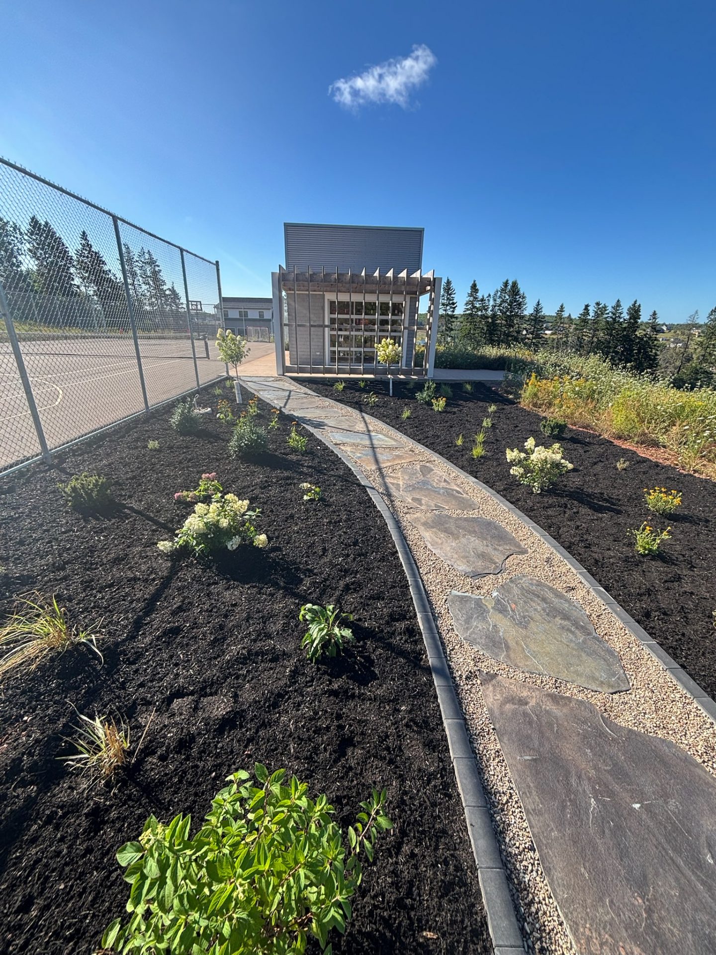 Garden path leading to modern pavilion, clear sky.