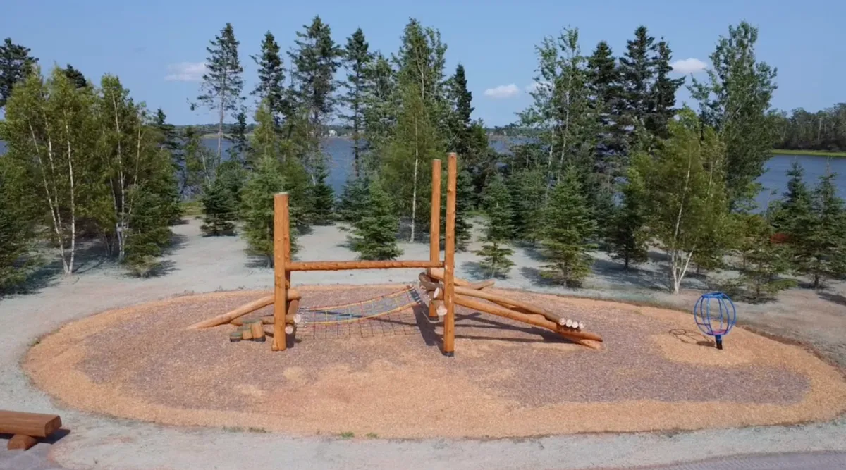 Wooden playground equipment near a lake and trees.