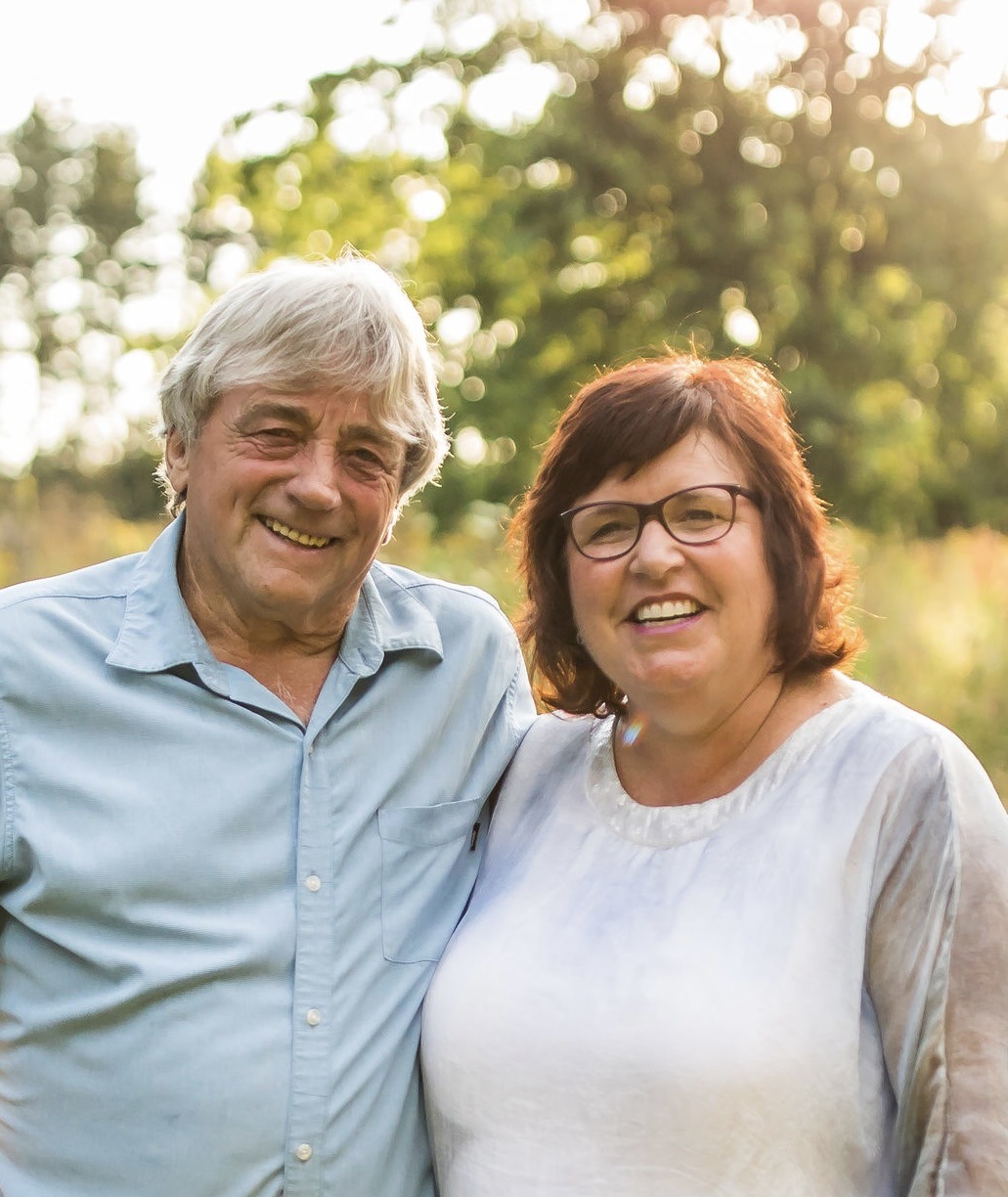 Smiling older couple outdoors with sunlight background.