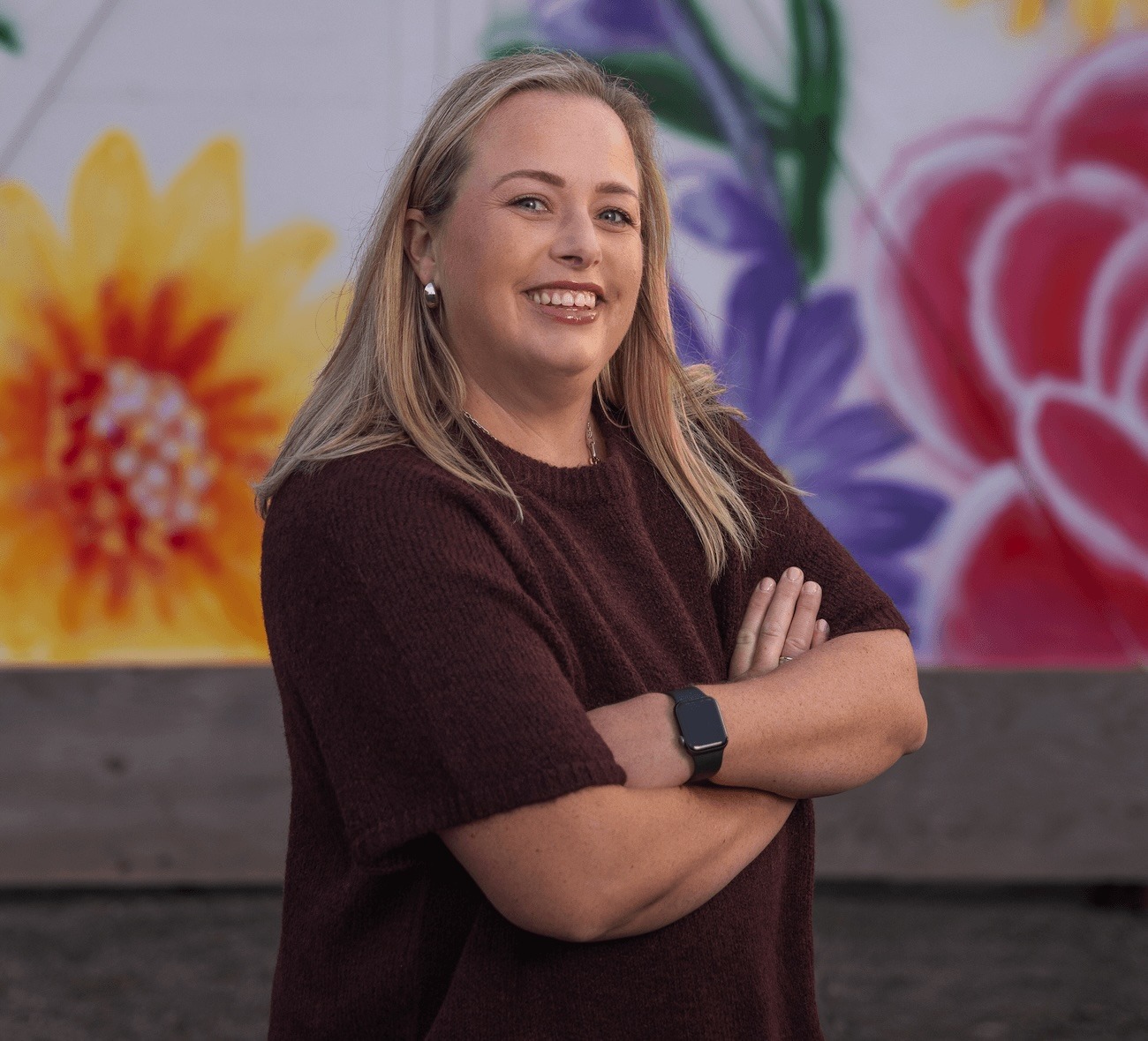 Smiling woman standing in front of colorful mural.