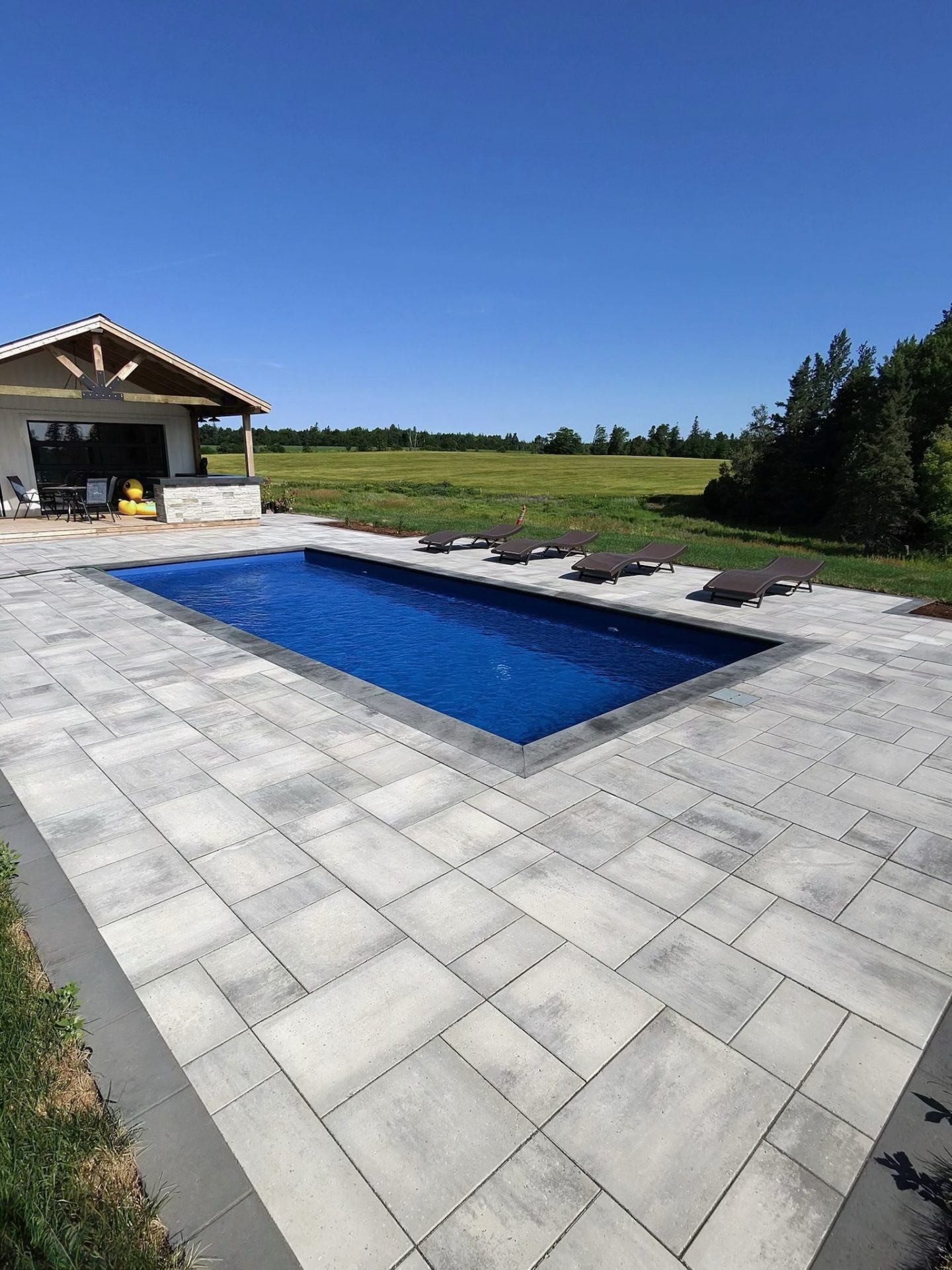 Modern poolside patio with loungers and a field view.